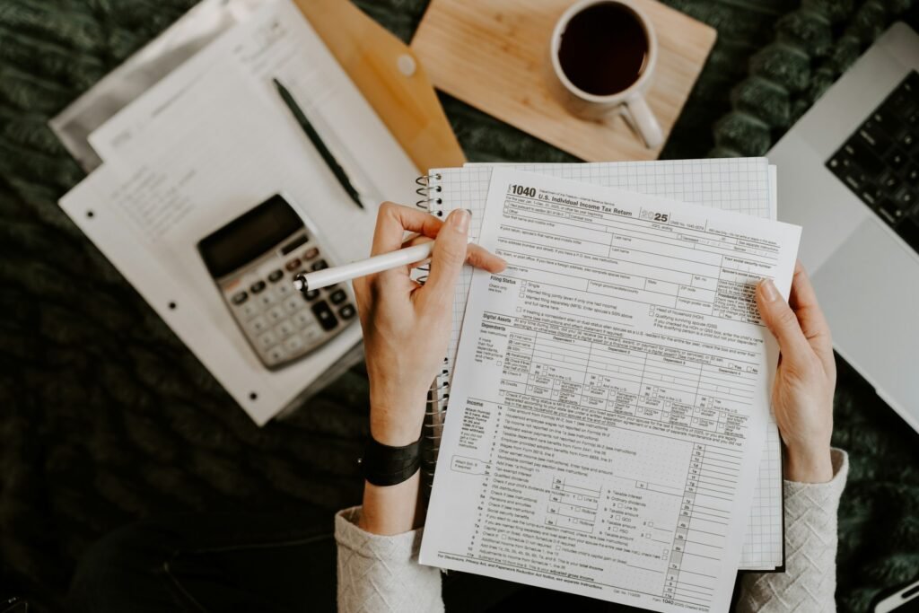 Person calculating figures on tax paperwork with a calculator, notebook, and coffee